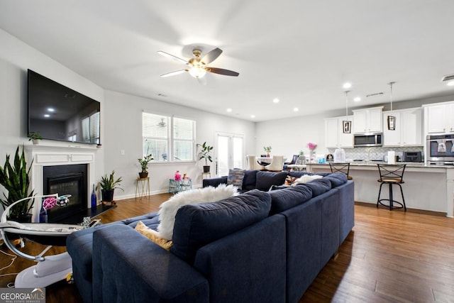 living area featuring baseboards, ceiling fan, recessed lighting, wood finished floors, and a glass covered fireplace