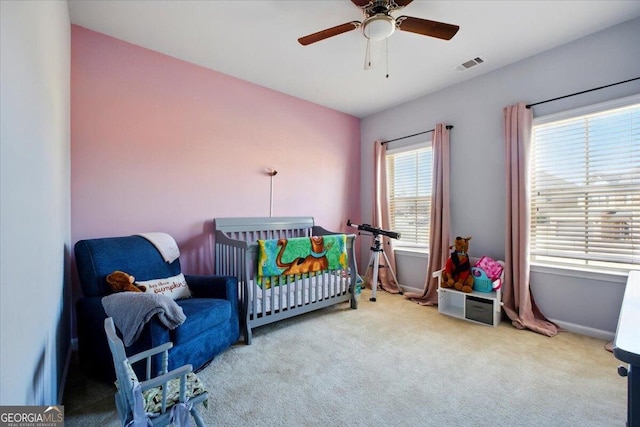 bedroom with visible vents, carpet floors, a nursery area, baseboards, and ceiling fan