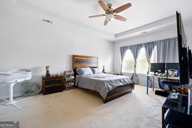 carpeted bedroom featuring visible vents, baseboards, a raised ceiling, and ceiling fan