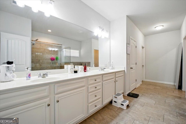 full bathroom with a tile shower, double vanity, baseboards, and a sink