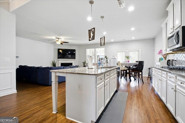 kitchen featuring ceiling fan, appliances with stainless steel finishes, a fireplace, wood finished floors, and a sink