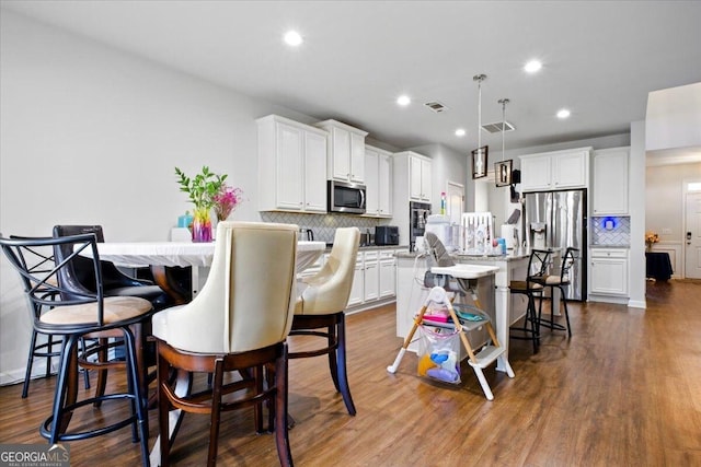 kitchen with dark wood-style floors, visible vents, white cabinetry, stainless steel appliances, and a kitchen bar