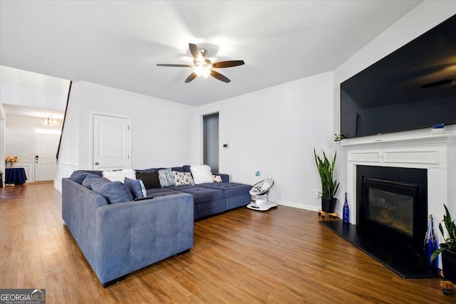 living area featuring a glass covered fireplace, baseboards, wood finished floors, and a ceiling fan