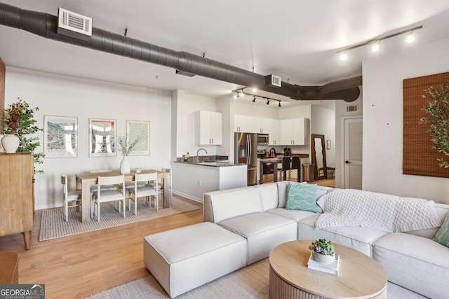 living area with rail lighting, light wood-style floors, and visible vents