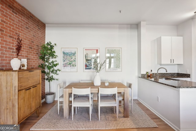 dining space with baseboards, wood finished floors, and brick wall