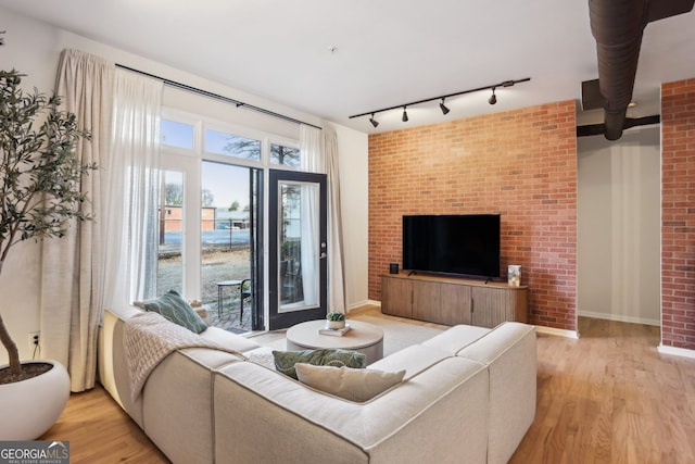 living area featuring track lighting, light wood-style floors, baseboards, and brick wall