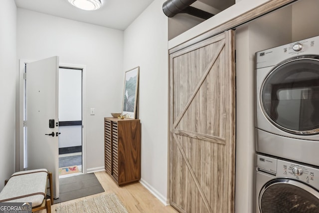 laundry area featuring light wood-style flooring, a barn door, stacked washer / dryer, baseboards, and laundry area