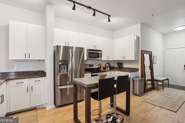 kitchen with stainless steel appliances, dark stone counters, light wood-style floors, and white cabinetry