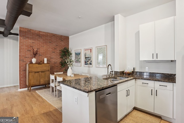 kitchen with dark stone countertops, a peninsula, stainless steel dishwasher, white cabinets, and a sink