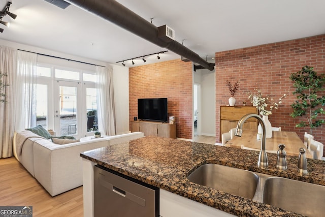 kitchen featuring brick wall, open floor plan, light wood-type flooring, stainless steel dishwasher, and a sink