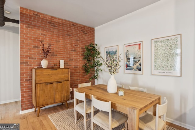 dining room with light wood-style flooring, baseboards, and brick wall