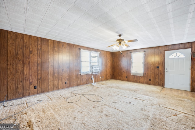 foyer entrance featuring carpet flooring, a ceiling fan, and wood walls