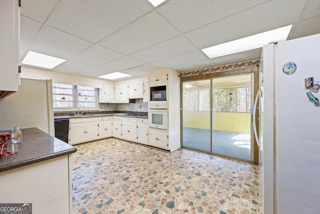 kitchen featuring black appliances, a sink, backsplash, dark countertops, and a paneled ceiling