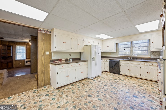 kitchen with dark countertops, wooden walls, black dishwasher, white fridge with ice dispenser, and a sink