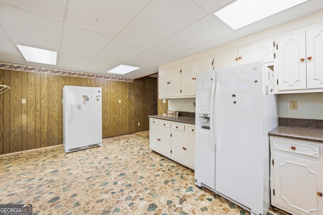 kitchen featuring dark countertops, wooden walls, white refrigerator with ice dispenser, and freestanding refrigerator