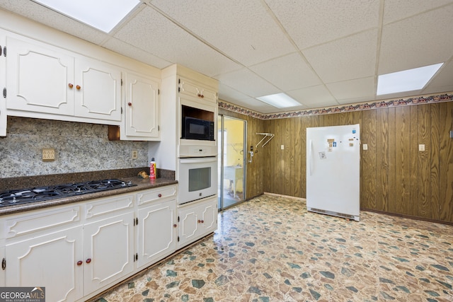 kitchen with white appliances, dark countertops, wood walls, and white cabinets