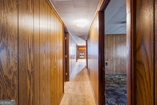 hall featuring wooden walls and light colored carpet