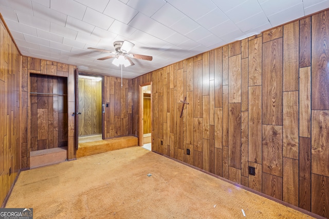 unfurnished bedroom with wooden walls, carpet floors, and ceiling fan