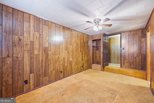 empty room featuring carpet flooring, wood walls, and a ceiling fan