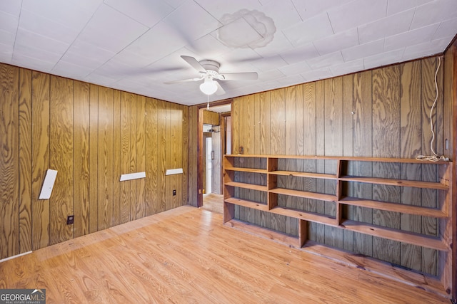 unfurnished room with wooden walls, ceiling fan, and wood finished floors