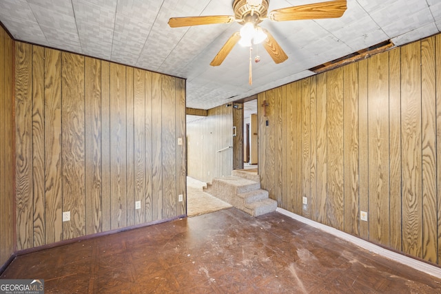 empty room featuring stairway, wood walls, a ceiling fan, and baseboards