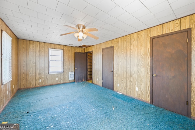 unfurnished bedroom with carpet flooring, wood walls, and a ceiling fan