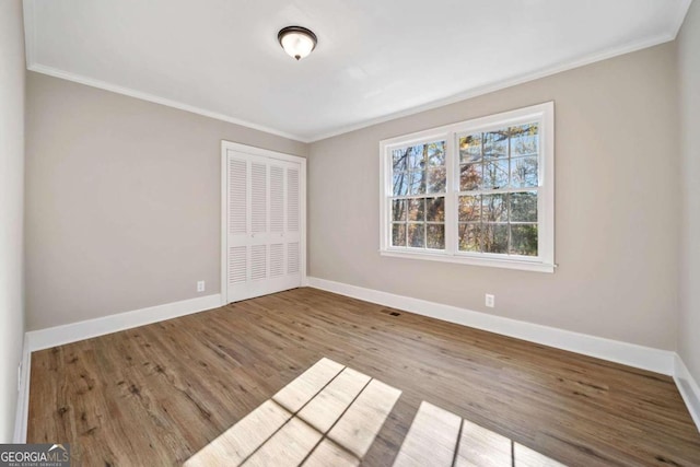 unfurnished bedroom featuring a closet, baseboards, wood finished floors, and crown molding