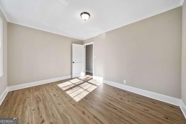 spare room featuring crown molding, wood finished floors, and baseboards