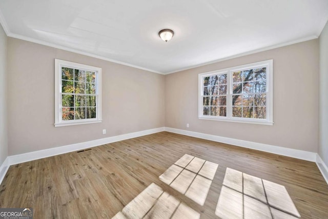 empty room with visible vents, baseboards, wood finished floors, and crown molding