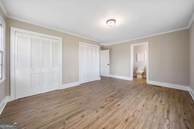 unfurnished bedroom featuring baseboards, two closets, wood finished floors, and crown molding