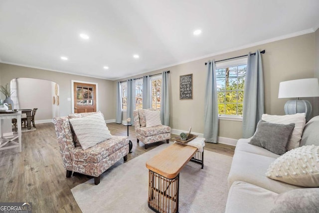 living area featuring crown molding, wood finished floors, arched walkways, and baseboards