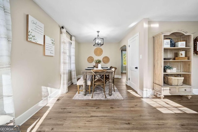 dining space with visible vents, baseboards, a chandelier, wood finished floors, and arched walkways