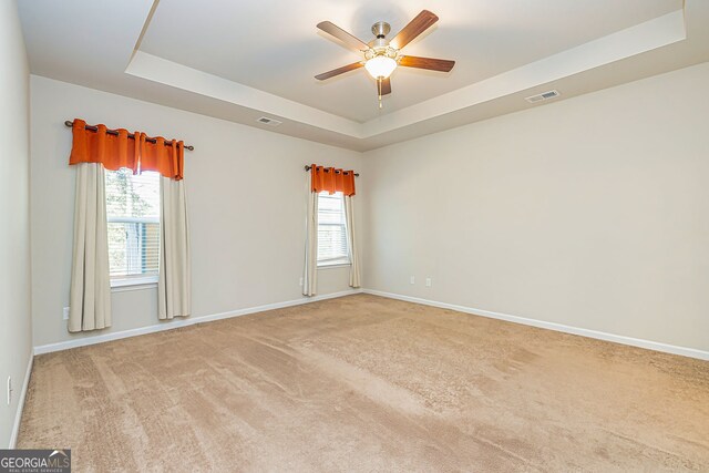 carpeted spare room with a tray ceiling, plenty of natural light, a ceiling fan, and visible vents