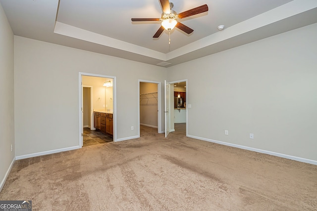 unfurnished bedroom with a walk in closet, a tray ceiling, connected bathroom, carpet, and baseboards