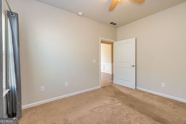 carpeted spare room with visible vents, baseboards, and a ceiling fan