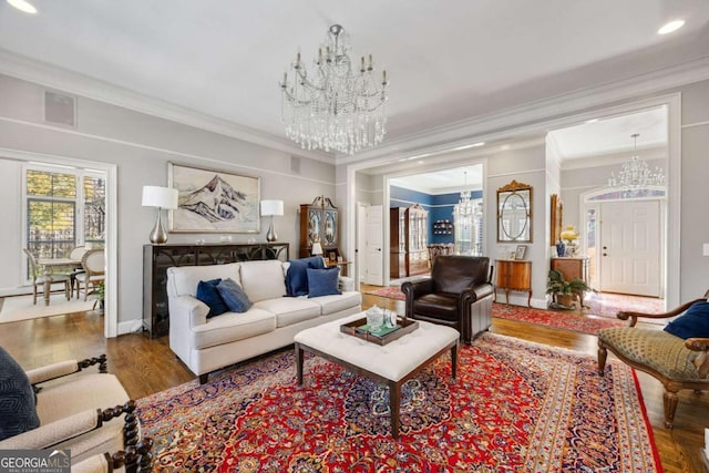 living area featuring visible vents, crown molding, baseboards, wood finished floors, and a notable chandelier