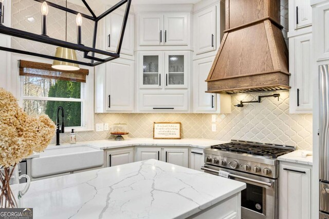 kitchen featuring a sink, white cabinets, high end range, and custom range hood