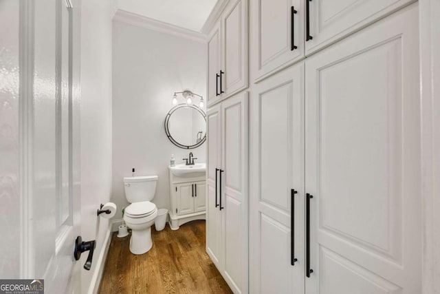 half bath featuring vanity, wood finished floors, baseboards, ornamental molding, and toilet