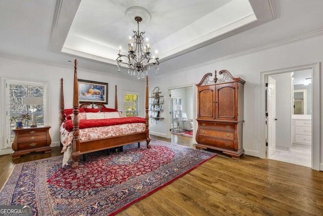 bedroom featuring light wood finished floors, connected bathroom, baseboards, ornamental molding, and a raised ceiling