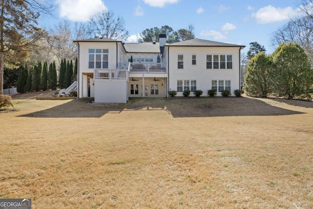 back of property featuring a wooden deck, stucco siding, a lawn, and a chimney