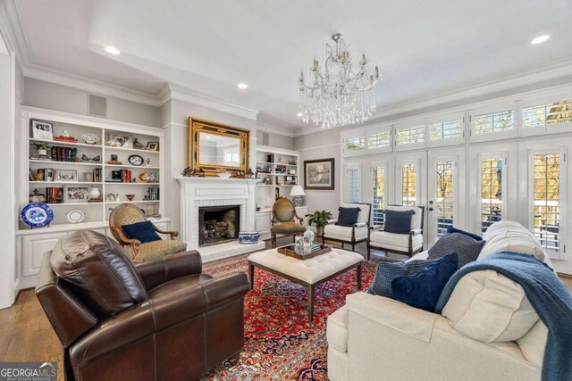 living area with a chandelier, a brick fireplace, wood finished floors, and ornamental molding