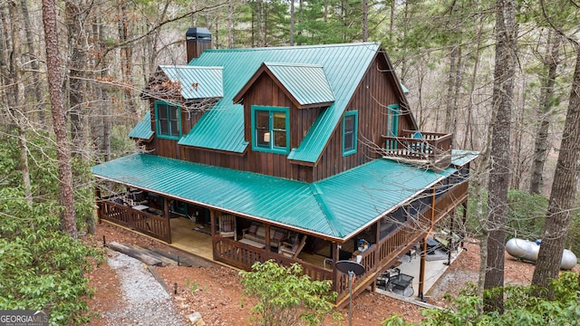 view of front of home with metal roof, a wooded view, and a chimney