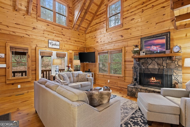 living room featuring wooden walls, a stone fireplace, visible vents, and hardwood / wood-style floors