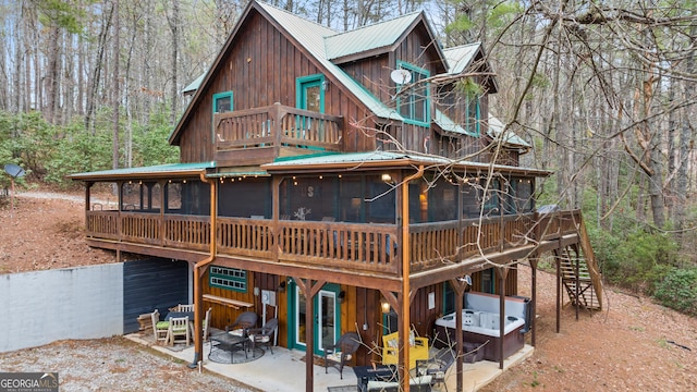 back of house featuring a wooded view, stairs, metal roof, a sunroom, and a patio area