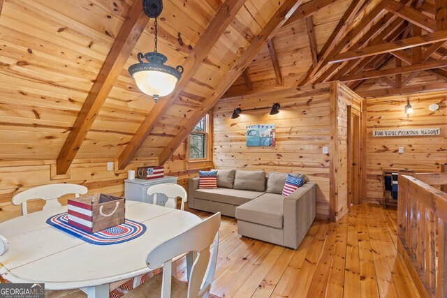 dining space with lofted ceiling with beams, wooden walls, wood ceiling, and light wood-type flooring