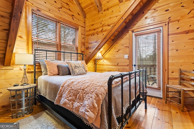 bedroom with vaulted ceiling, wooden walls, multiple windows, and access to outside