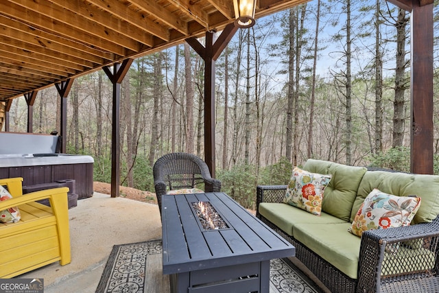 view of patio featuring a forest view, an outdoor living space with a fire pit, and a hot tub