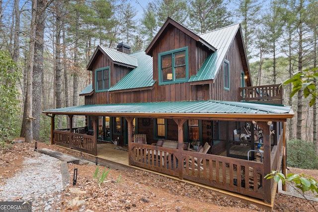 back of house featuring metal roof, board and batten siding, a porch, and a chimney