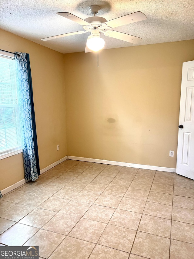 empty room featuring light tile patterned floors, baseboards, a textured ceiling, and ceiling fan