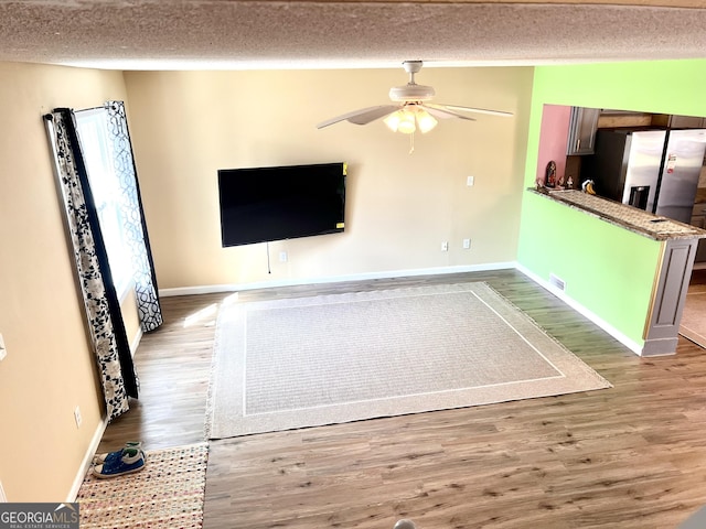 unfurnished living room featuring baseboards, a textured ceiling, ceiling fan, and wood finished floors